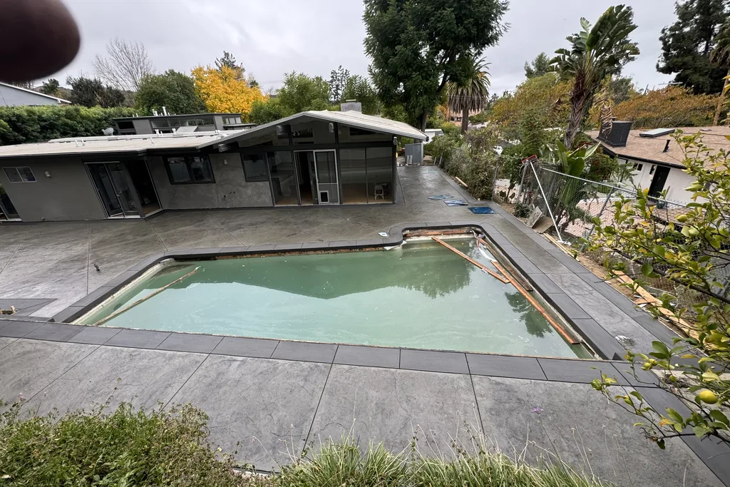Pool deck and coping in grey concrete beside a mid-century house